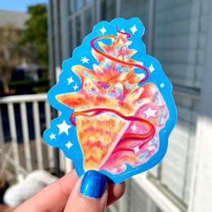 Peut inclure: Un autocollant coloré représentant un coquillage aux tons orange, rose et jaune, orné d'un ruban rouge et d'étoiles blanches, sur un fond bleu vif.