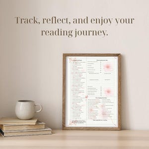 May include: A wooden-framed print with text that reads "Track, reflect, and enjoy your reading journey." The print has a floral design and lists reading challenges and prompts. A stack of books and a ceramic mug sit on a wooden surface.