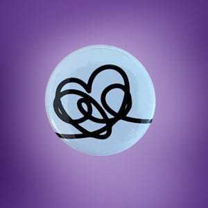 Peut inclure: Un bouton rond bleu clair avec un motif de cœur noir abstrait. Le chiffre "1" est imprimé en noir en bas du bouton. Le bouton est posé sur un fond dégradé violet.