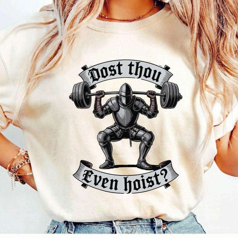 May include: Cream-colored t-shirt featuring a graphic of a knight in armor lifting a barbell. The text "Dost thou" is above the barbell, and "Even hoist?" is below. The knight is in a squat position, with the barbell resting on their shoulders.