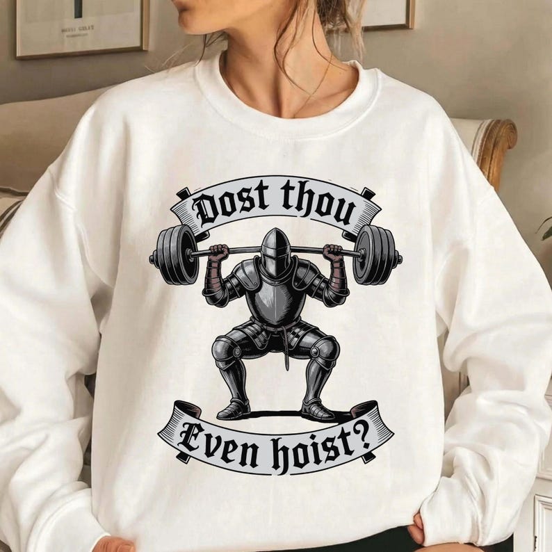 May include: White sweatshirt featuring a graphic of a knight lifting a barbell. The knight is in full armor, squatting with the weight overhead. Text on banners reads "Dost thou" and "Even hoist?"