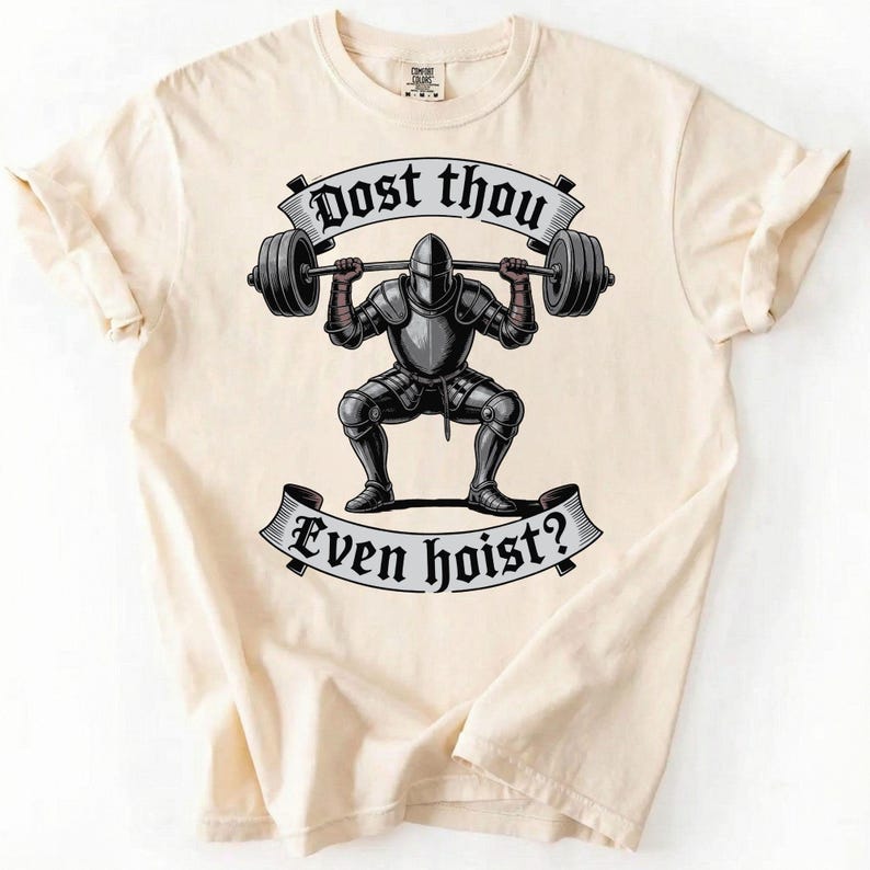 May include: Cream-colored t-shirt featuring a graphic of a knight lifting a barbell. The knight is in full armor, squatting with the weight. The text "Dost thou Even hoist?" is above and below the knight in a banner.