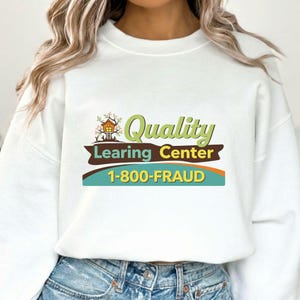 Puede incluir: Sudadera blanca con el texto "Quality Learing Center" en verde y marrón, con un gráfico de casa en el árbol. Debajo del texto está el número de teléfono "1-800-FRAUD" en amarillo. La sudadera la lleva una persona.