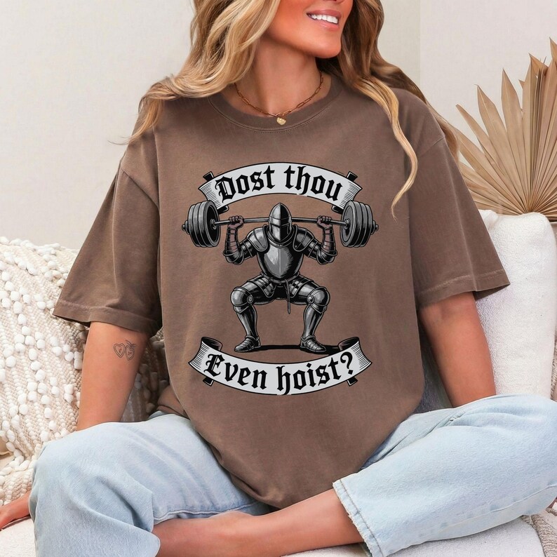 May include: Brown t-shirt featuring a graphic of a knight lifting a barbell. The text on the shirt reads "Dost thou even hoist?" in a banner design. The knight is in full armor.