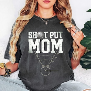 May include: Dark gray t-shirt with the text "SHOT PUT MOM" in white block letters. A graphic of a shot put ball is above the text. Below the text is a diagram with measurements.