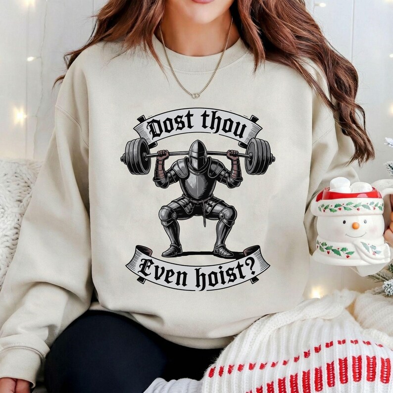 May include: A beige sweatshirt featuring a graphic of a knight lifting a barbell. The knight is in full armor, squatting with the weight overhead. The text on the sweatshirt reads "Dost thou Even hoist?"