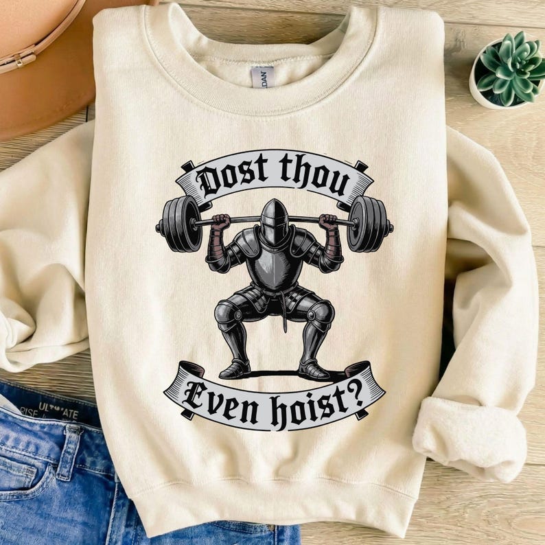 May include: Cream-colored sweatshirt with a graphic of a knight lifting weights. The knight is in full armor, and the text "Dost thou Even hoist?" is displayed above and below the knight in a banner.