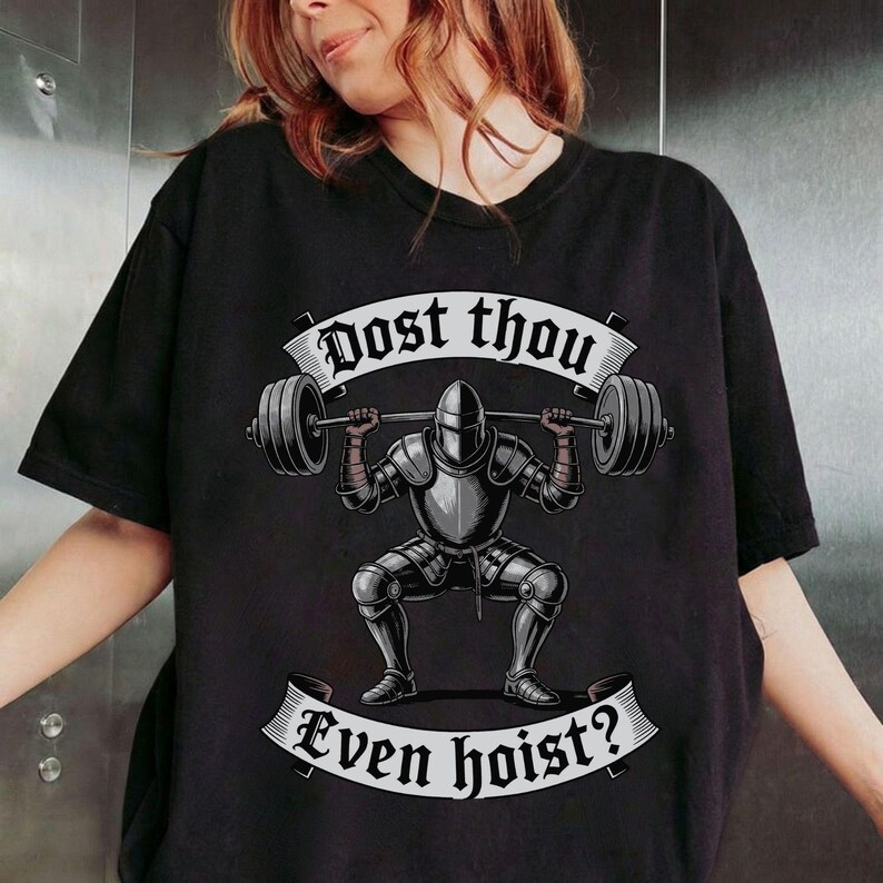 May include: Black t-shirt featuring a knight lifting a barbell in a squat position. The knight is clad in silver armor. The text "Dost thou" is above the knight, and "Even hoist?" is below.