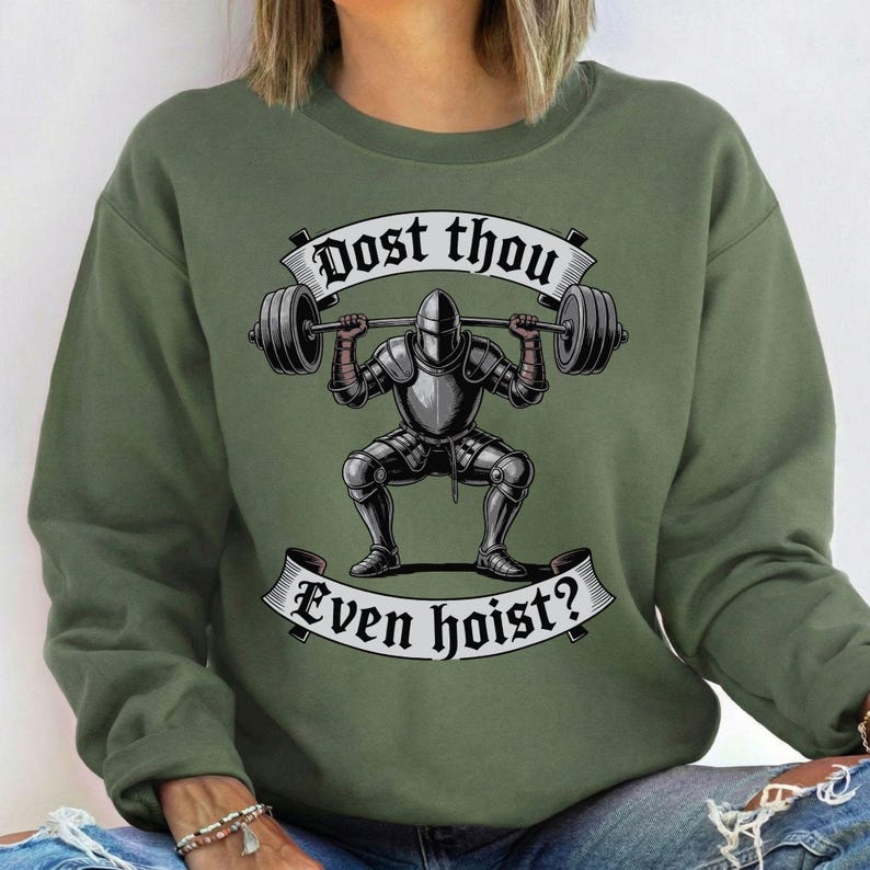 May include: Olive green sweatshirt with a graphic of a knight lifting a barbell. The knight is wearing full armor and is in a squat position. The text "Dost thou even hoist?" is displayed above and below the knight in a banner.