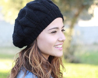 May include: A woman with long brown hair is wearing a black knitted beret. She is smiling and looking to the right.