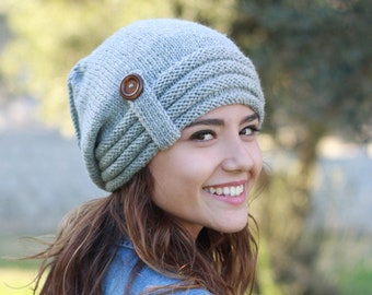 May include: A gray knitted beanie with a button detail. The beanie is folded down on one side and has a slouchy fit.