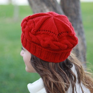 Può includere: Un cappello rosso brillante lavorato a maglia con un motivo a trecce. Il cappello è realizzato con un filato morbido e strutturato e presenta un motivo dettagliato. Un accessorio caldo per il clima freddo.