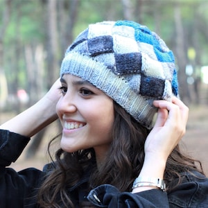 May include: A woman wearing a black jacket with a blue and grey checkered knit beanie. The beanie has a unique woven pattern.