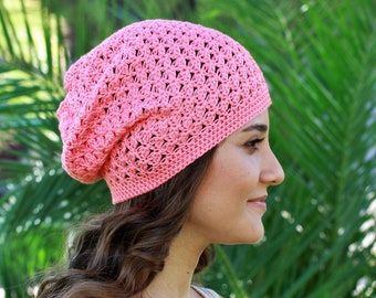 May include: A pink crocheted beanie with a lacy pattern. The beanie is worn by a person with long brown hair.