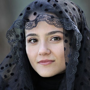 May include: A portrait of a person wearing a black veil with a polka dot pattern. The veil has a decorative lace trim along the edge. The person is looking directly at the camera.