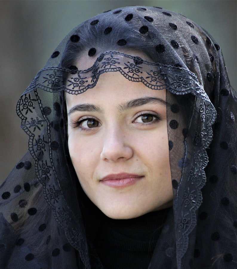 May include: A portrait of a person wearing a black veil with a polka dot pattern. The veil has a decorative lace trim along the edge. The person is looking directly at the camera.