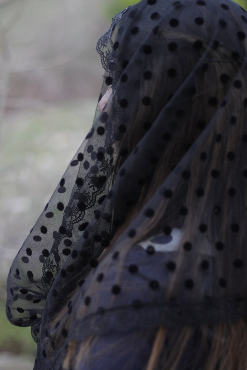 May include: A black veil with a polka dot pattern and lace trim. The sheer fabric drapes over the head and shoulders. The veil is a dark, elegant accessory.