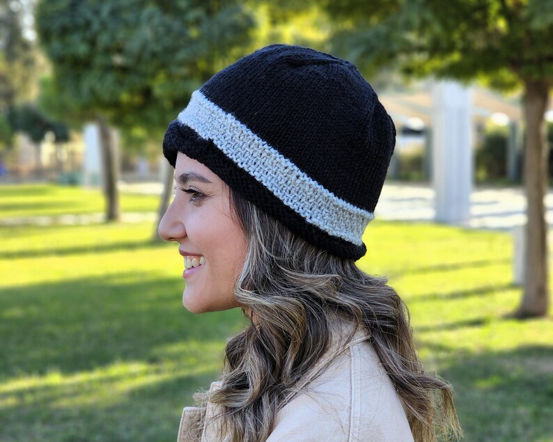 May include: A black knit beanie with a white stripe around the brim. The beanie is worn by a person with long brown hair.