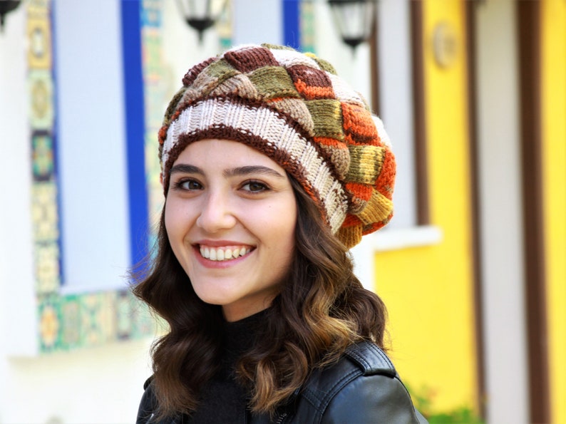 May include: A woman wearing a brown, white, orange, and green knitted beret with a geometric pattern.