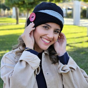 May include: A black and gray knit hat with a red button. The hat has a wide brim and a slouchy fit.