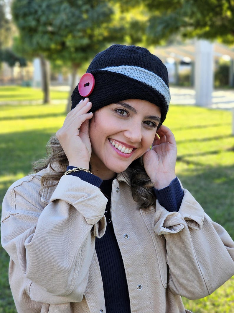 May include: A black and gray knit hat with a red button. The hat has a wide brim and a slouchy fit.