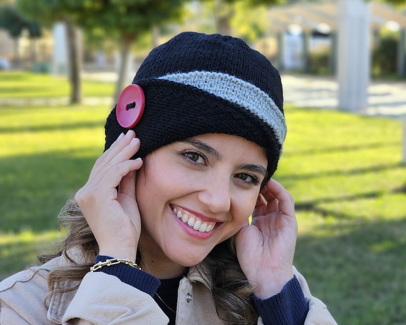 May include: A black knit beanie with a gray stripe and a red button. The beanie is slouchy and has a wide brim.