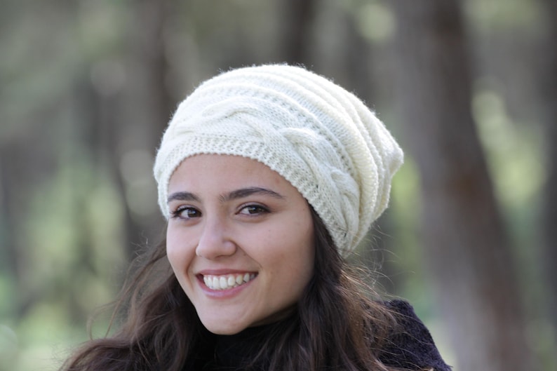 Pode incluir: Um gorro de malha creme com um design de malha entran&ccedil;ada. O chap&eacute;u &eacute; feito de um fio macio e texturizado e tem um ajuste confort&aacute;vel e folgado. Este chap&eacute;u de inverno &eacute; perfeito para se manter aquecido em climas frios.