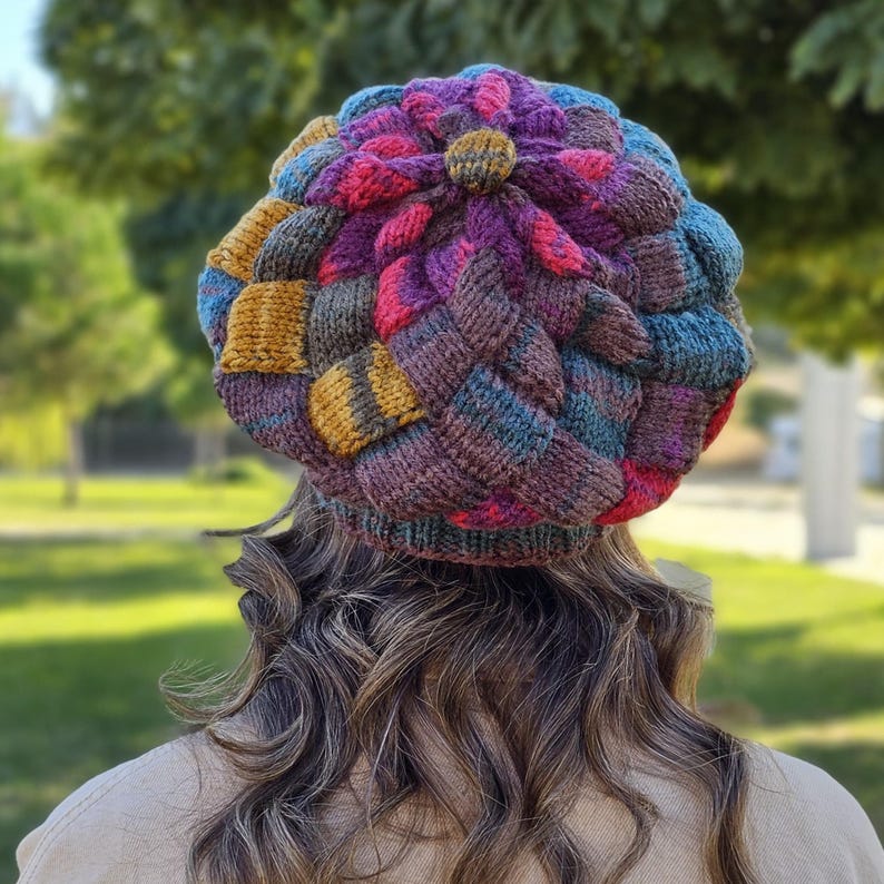 May include: A colourful knitted hat with a flower design on top. The hat is made with a variety of colours, including purple, pink, blue, and brown.