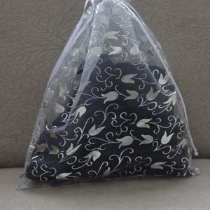 May include: A dark gray decorative pillow with a silver floral pattern is enclosed in a sheer white gift bag. The bag is gathered at the top with a white ribbon, creating a soft, elegant presentation.