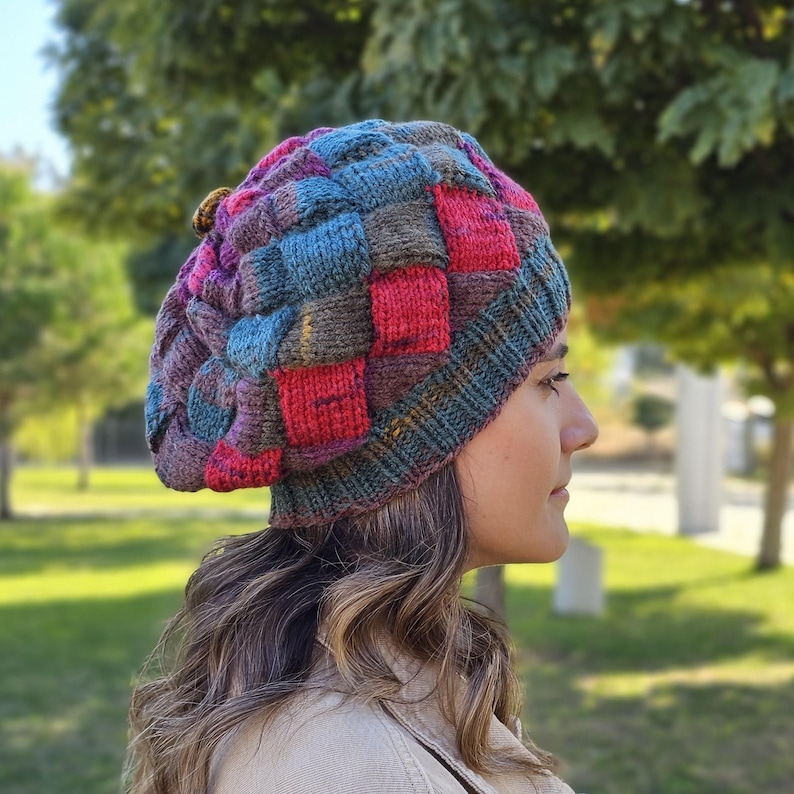 May include: A colourful knitted beret with a patchwork design in shades of red, blue, green, and brown. The beret has a textured, woven look and a small button on top.