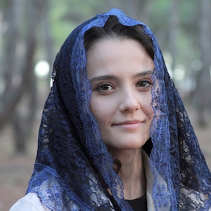 May include: A woman wearing a blue lace veil over her head and shoulders. The veil is delicate and intricate, with a floral pattern. The woman is looking at the camera with a soft smile.
