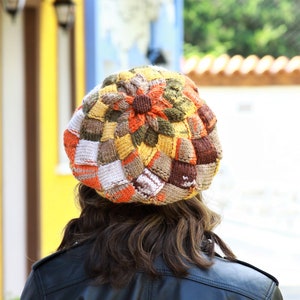 May include: A colorful knitted beret with a patchwork design in shades of brown, orange, white, and yellow.