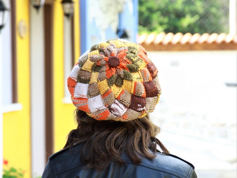 May include: A colorful knitted beret with a patchwork design in shades of brown, orange, white, and yellow.
