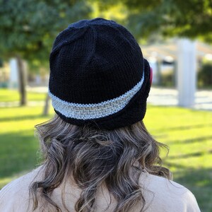 May include: A black knitted hat with a gray trim. The hat has a curved brim and is worn on the back of the head.