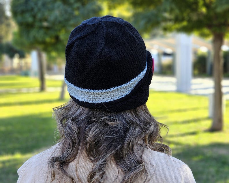 May include: A black knitted hat with a gray trim. The hat has a curved brim and is worn on the back of the head.