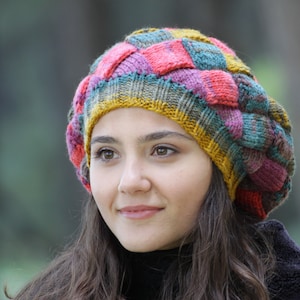May include: A woman wearing a colourful knitted hat with a patchwork design. The hat is made of various shades of pink, red, yellow, green, and blue yarn.