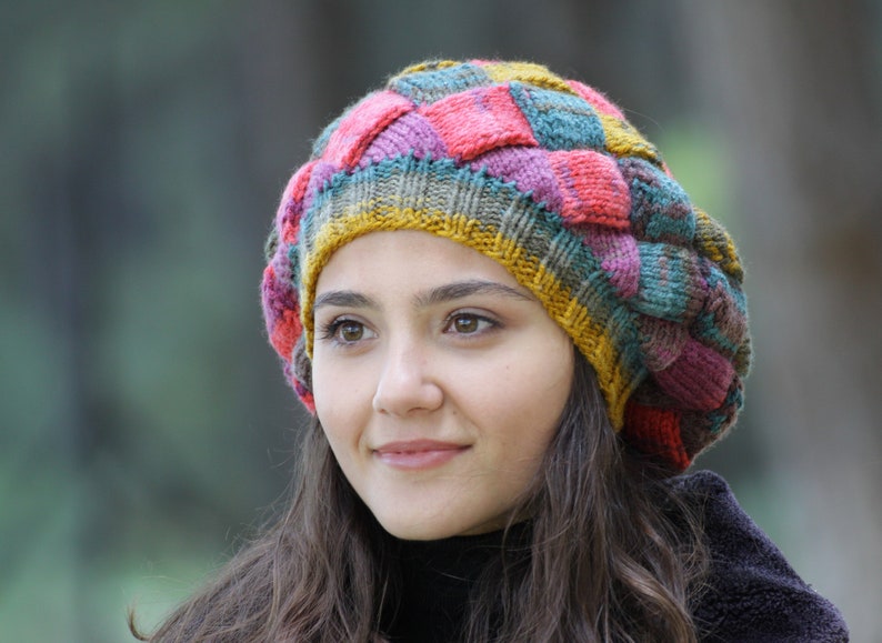 May include: A woman wearing a colourful knitted hat with a patchwork design. The hat is made of various shades of pink, red, yellow, green, and blue yarn.