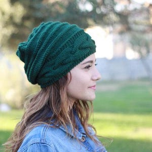 Pode incluir: Um gorro de malha verde escuro com um design de malha de cabo. O chap&eacute;u &eacute; feito de um fio macio e texturizado. Um acess&oacute;rio elegante para o clima frio.