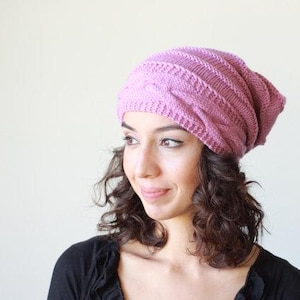 Pode incluir: Um gorro de malha na cor rosa empoeirado. O gorro apresenta um design de malha entran&ccedil;ada e &eacute; feito de um fio espesso e quente. Este gorro folgado &eacute; um acess&oacute;rio de moda para o inverno.