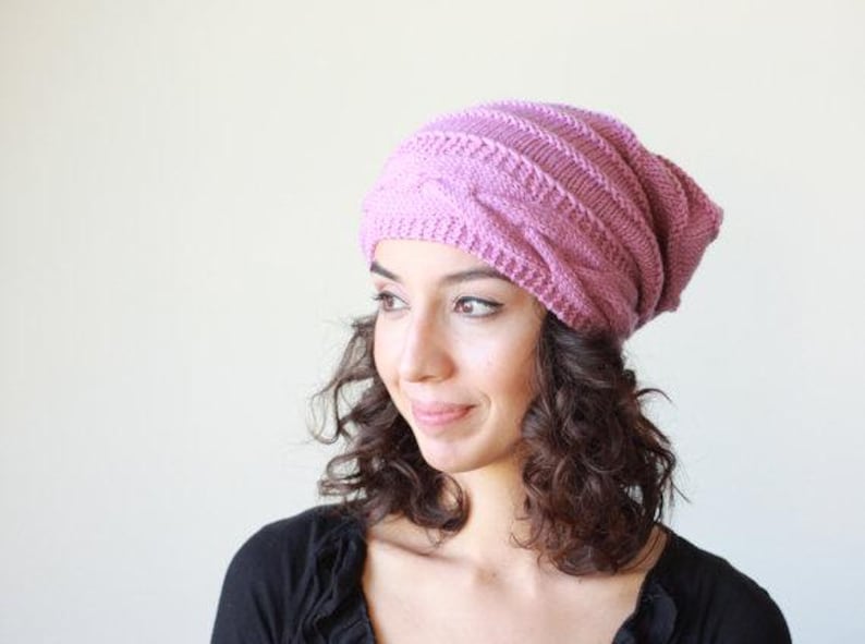 Pode incluir: Um gorro de malha na cor rosa empoeirado. O gorro apresenta um design de malha entran&ccedil;ada e &eacute; feito de um fio espesso e quente. Este gorro folgado &eacute; um acess&oacute;rio de moda para o inverno.