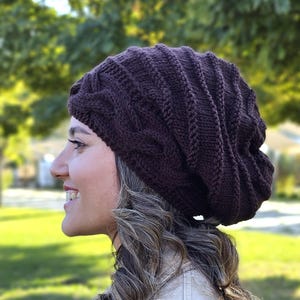 Pode incluir: Um gorro de malha castanho escuro com um design de malha entran&ccedil;ada. O chap&eacute;u &eacute; feito de um fio macio e texturizado e tem um ajuste folgado. Um acess&oacute;rio quente e elegante para o clima frio.