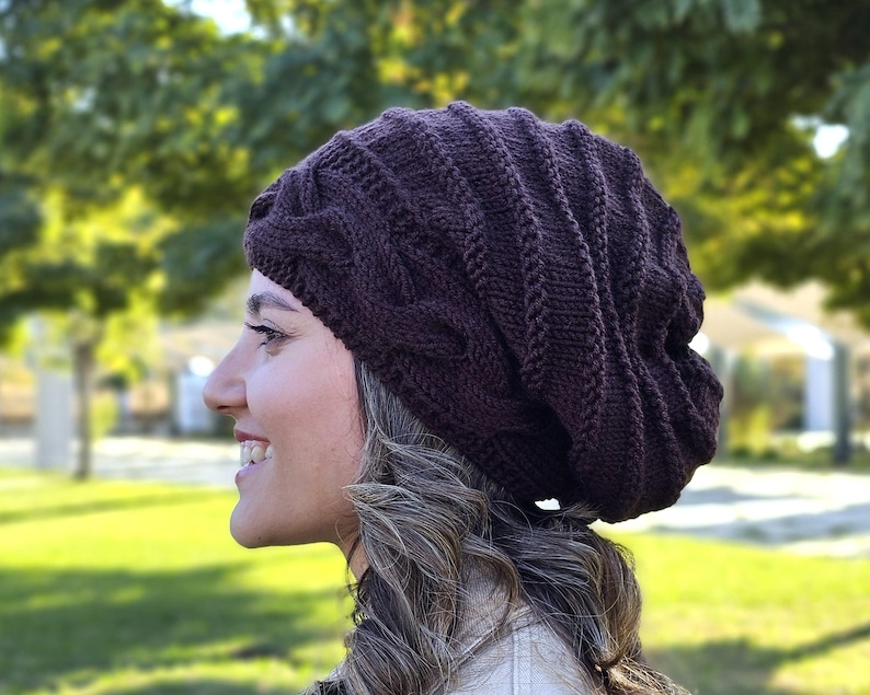 Pode incluir: Um gorro de malha castanho escuro com um design de malha entran&ccedil;ada. O chap&eacute;u &eacute; feito de um fio macio e texturizado e tem um ajuste folgado. Um acess&oacute;rio quente e elegante para o clima frio.