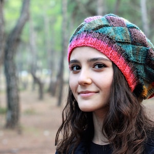 May include: A young person with long brown hair wearing a colourful knitted hat with a pink, green and brown pattern. The hat is a beret style with a wide brim.
