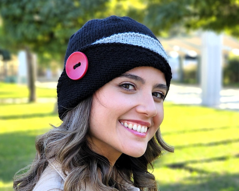 May include: A black and gray knitted hat with a red button. The hat has a wide brim and is angled slightly to the side.