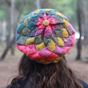 May include: A colourful knitted hat with a flower design. The hat is made of different shades of pink, yellow, green, and brown yarn.