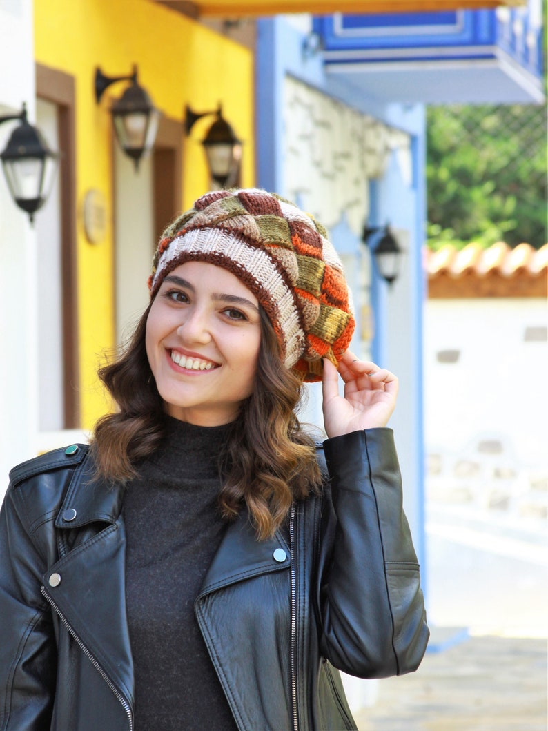 May include: A woman wearing a brown, orange, and white knitted beret with a black leather jacket.