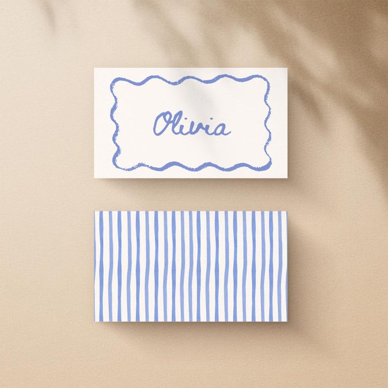 May include: Two rectangular cards. The top card has a blue wavy border and the name "Olivia" in blue script. The bottom card has a pattern of vertical blue stripes on a white background. The cards are on a beige surface.