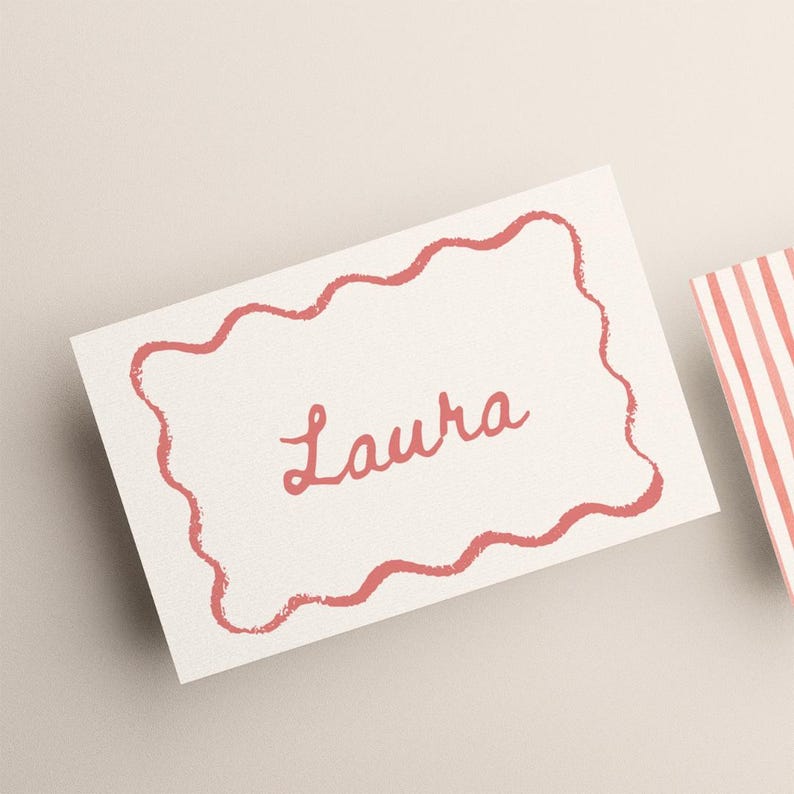 May include: A white place card with a wavy, coral-colored border and the name "Laura" in a matching script font. A second card with coral and white stripes is partially visible.