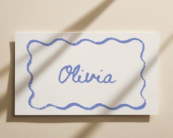 May include: A rectangular white card with a blue wavy border and the name "Olivia" in cursive script. The card is set against a neutral background with a shadow.