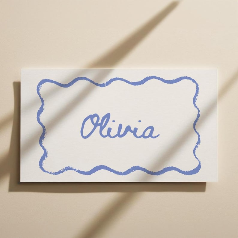May include: A rectangular white card with a blue wavy border and the name "Olivia" in cursive script. The card is set against a neutral background with a shadow.